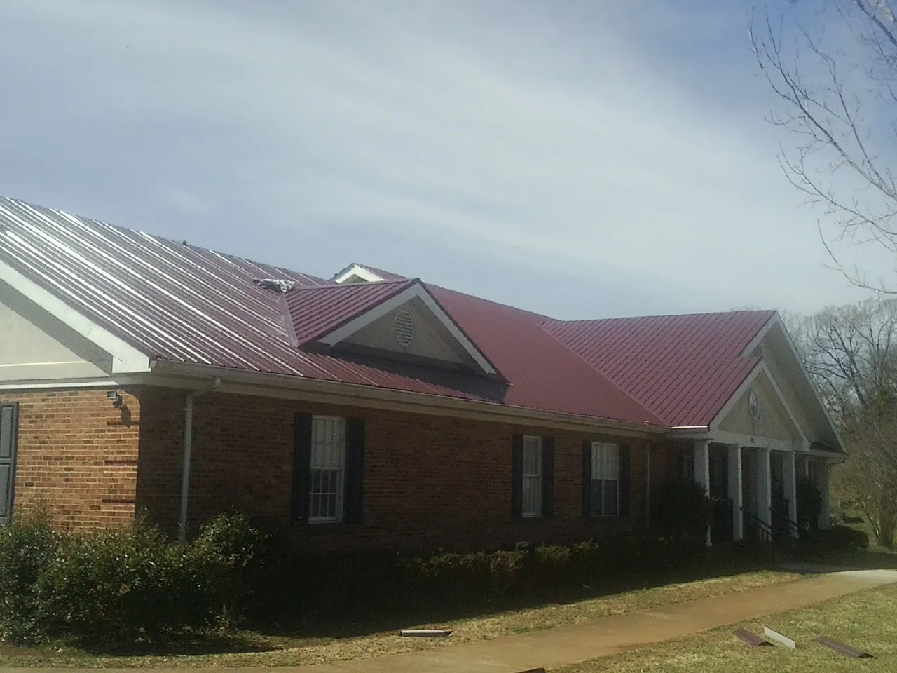 Red metal roof with gabled entries on a long brick building, from a Hail Damage Roof Repair job in Baconton