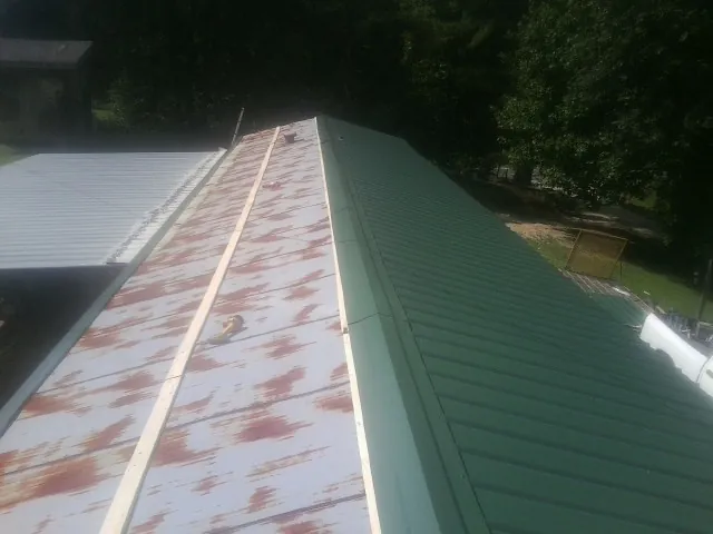 Old rusted panels beside newly installed green metal roofing — Wind Damage Roof Repair by Roofing Brothers in Baconton