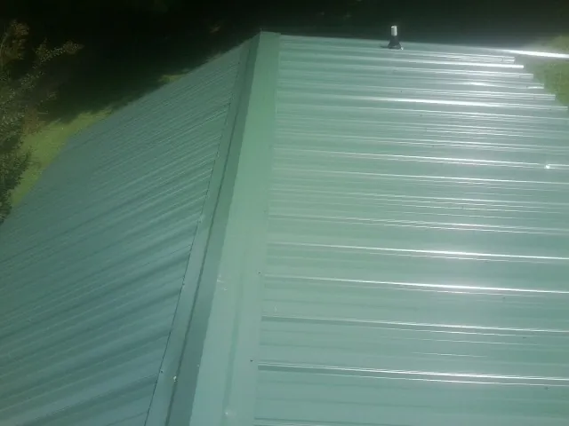 New green metal panels meeting at the ridge of a roof — Flat Roof Repair work by our crew in Baconton