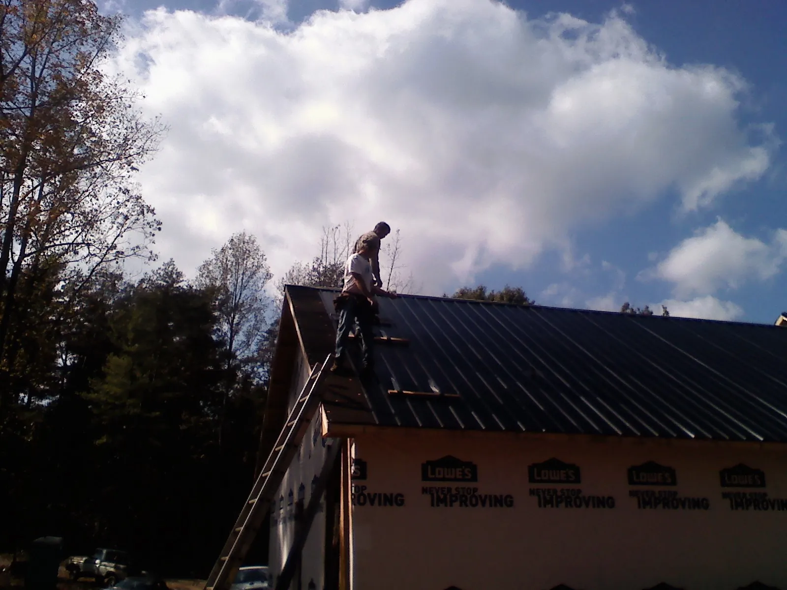 Roofer fastening dark metal panels high against a cloudy sky, from a Roof Inspection job in Baconton