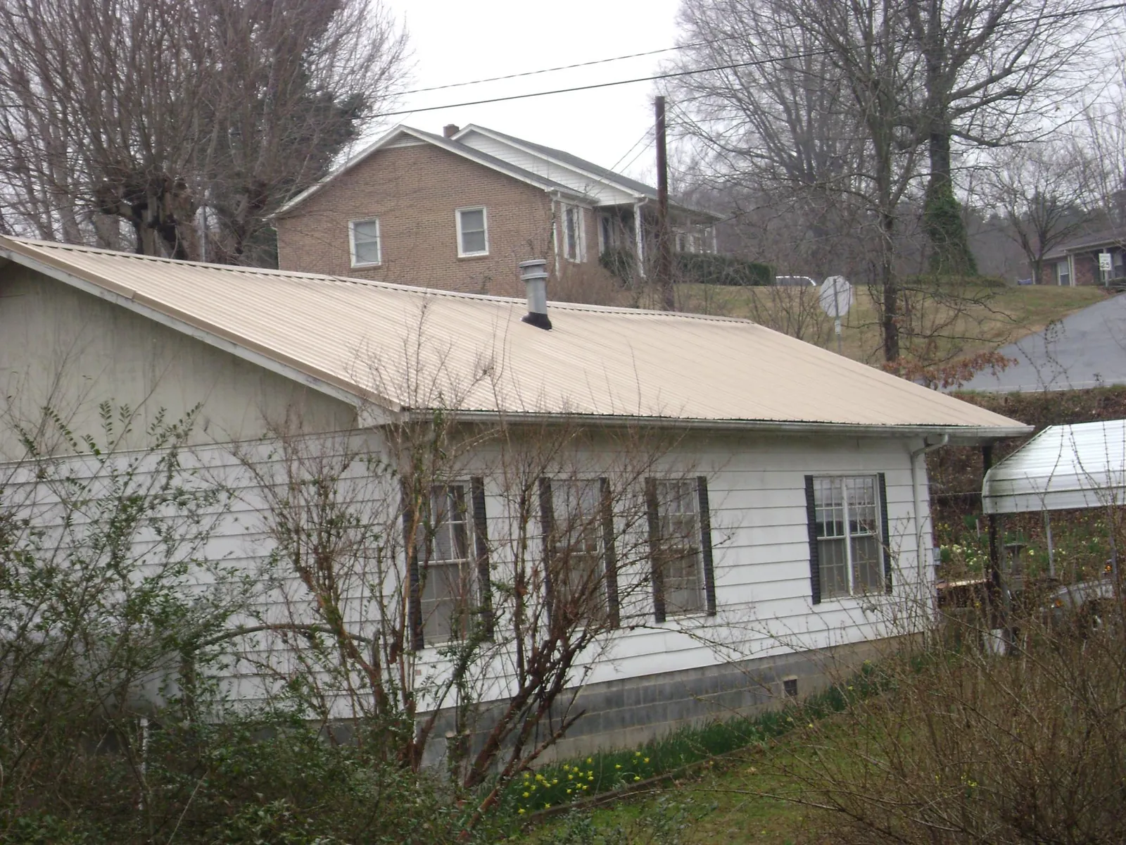 Tan metal roof on a white sided house set into a hillside — Commercial Roofing by Roofing Brothers in Baconton